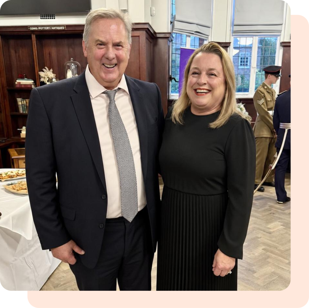 A man in a suit and tie and a woman in a black pleated dress standing together at an event.