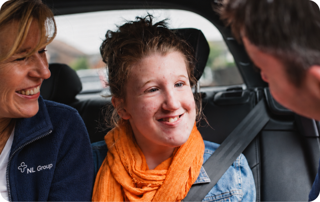 A young woman wearing an orange scarf sits in the back of a car between two people who are looking at her and smiling.
